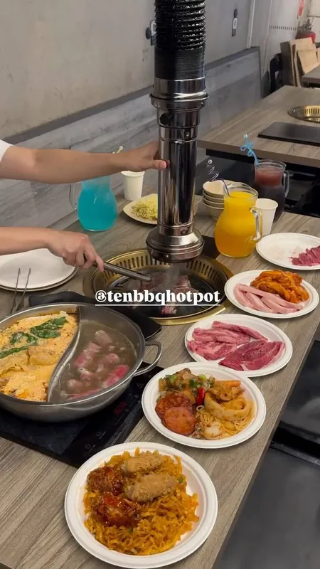 Sizzling tabletop grill surrounded by plates of meat and sides